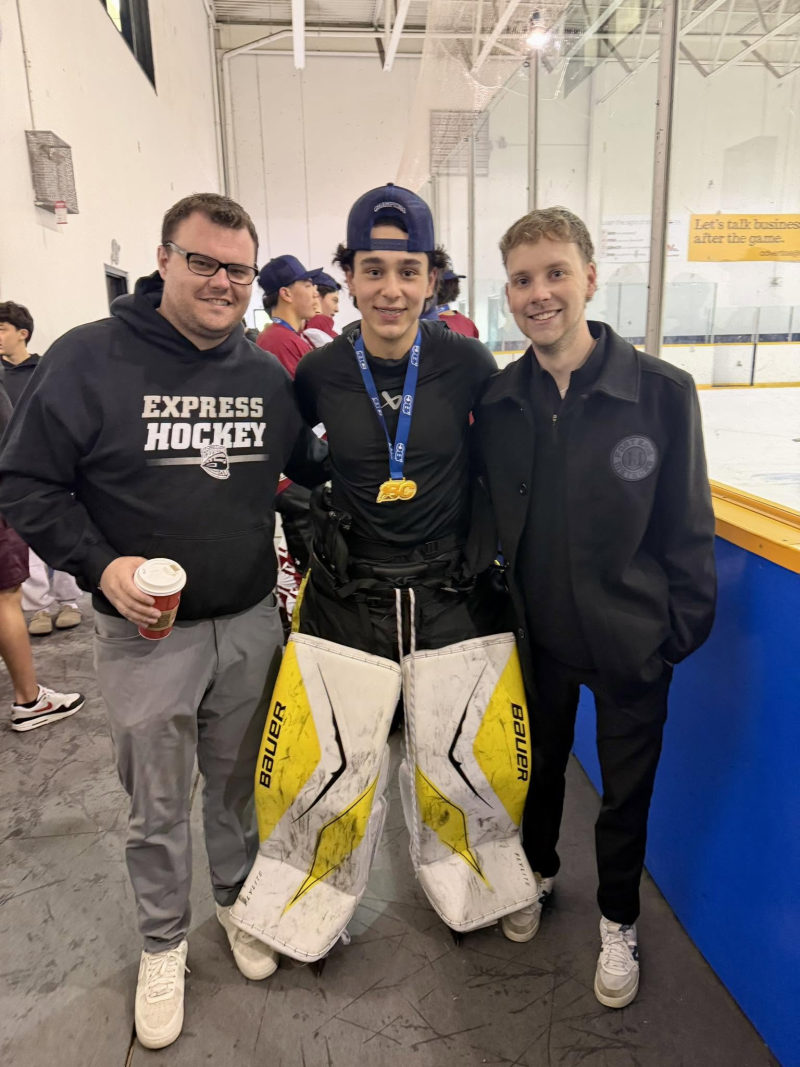A goalie in Bauer pads with a gold medal posing with friends in Express Hockey apparel at the rink.