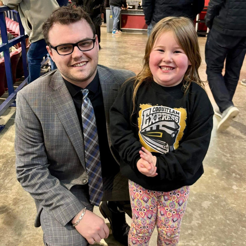 Tali Campbell kneeling beside a young girl in a Coquitlam Express sweatshirt at the arena concourse.