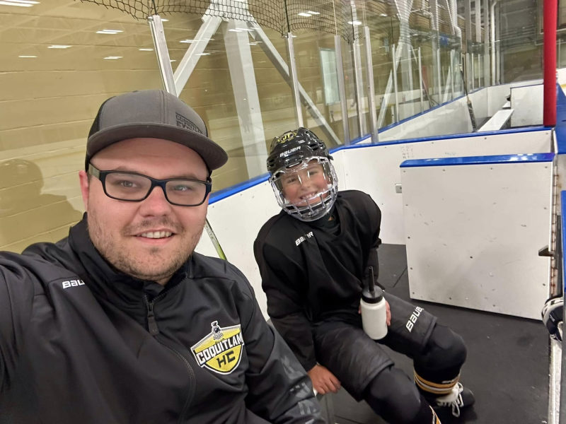 Tali Campbell in a Coquitlam HC jacket taking a selfie with a young hockey player in full gear on the bench.