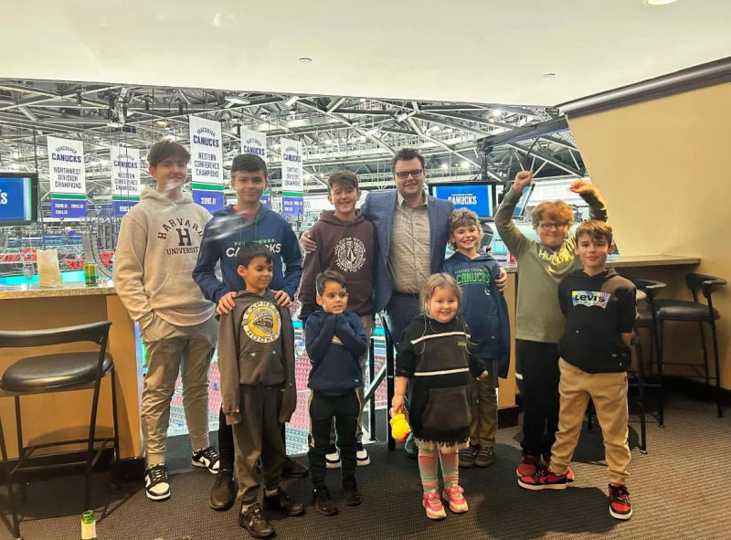 Tali Campbell with children and teens posing in a Vancouver Canucks arena beneath championship banners.
