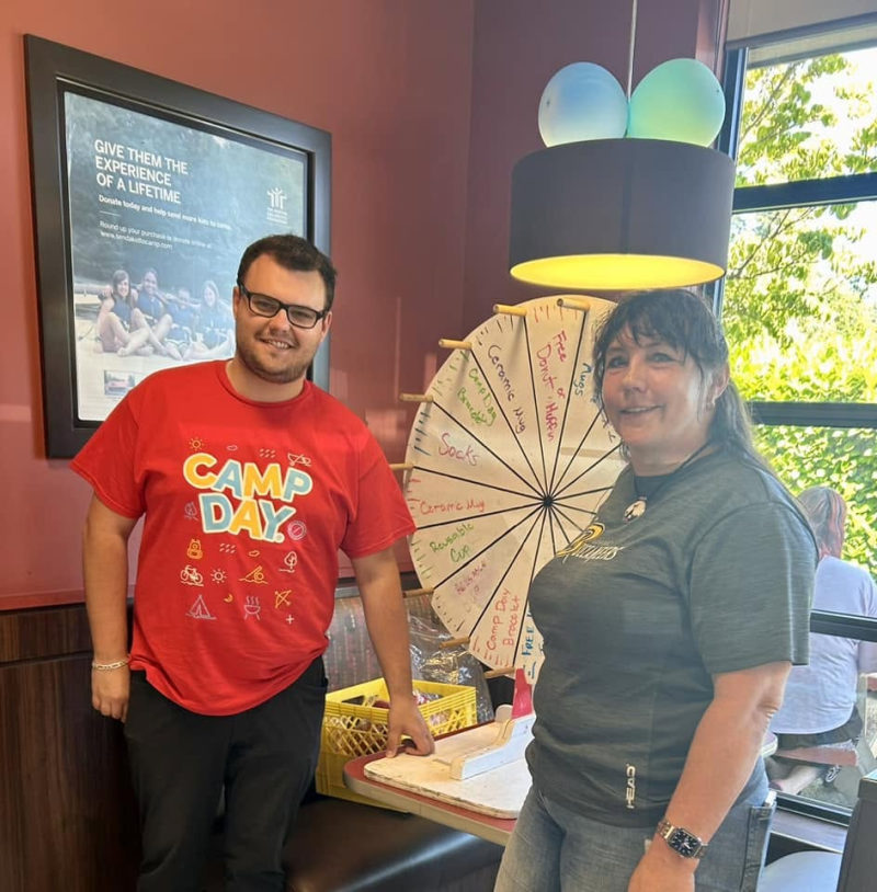 Tali Campbell beside a Tim Hortons Camp Day prize wheel with a store teammate.