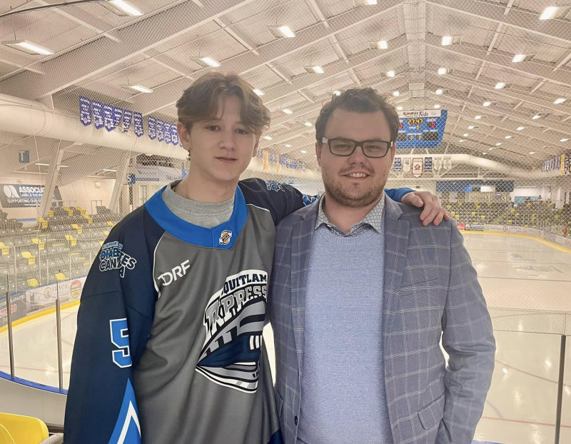 A Coquitlam Express player in jersey number 5 with Tali Campbell in a plaid blazer on the ice.
