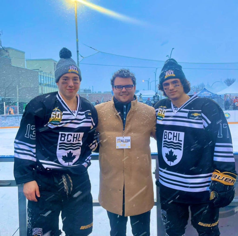 Two BCHL all-star players in white jerseys with a VIP guest at a snowy outdoor rink during the All-Star Weekend.