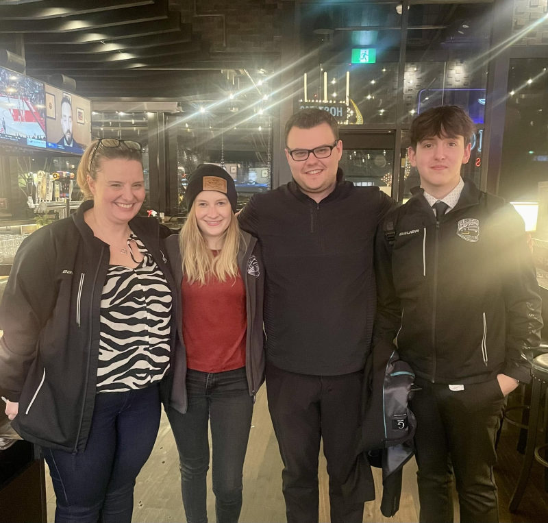 Four people smiling together at a restaurant or sports bar gathering.