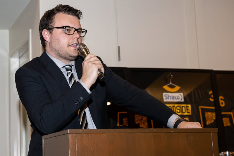 Tali Campbell in a suit speaking into a microphone at a wooden podium.