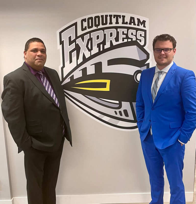 Two men in suits posing in front of the large Coquitlam Express train logo.