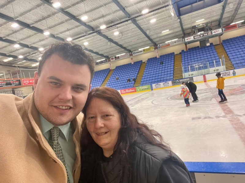 Tali Campbell in a tan coat taking a selfie with a colleague during public skate at an arena.