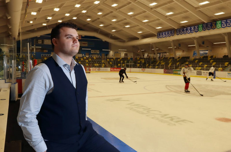 Tali Campbell in a navy vest leaning on the arena railing and looking out over the ice during a practice.