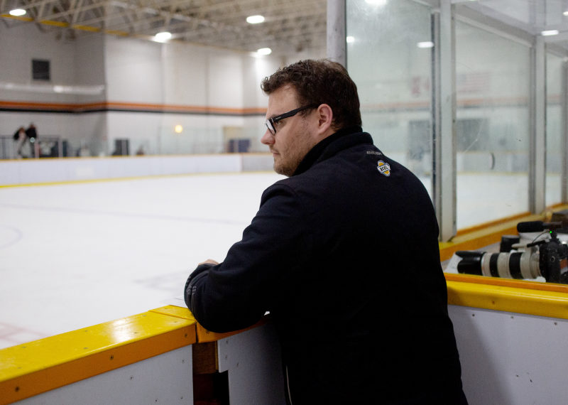 Tali Campbell in a BCHL jacket leaning on the rink boards and looking across the ice.