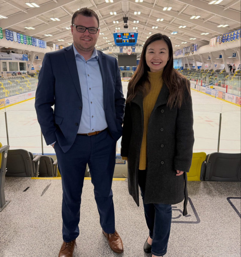 Tali Campbell in a blue suit standing with a community partner in the arena concourse overlooking the rink.